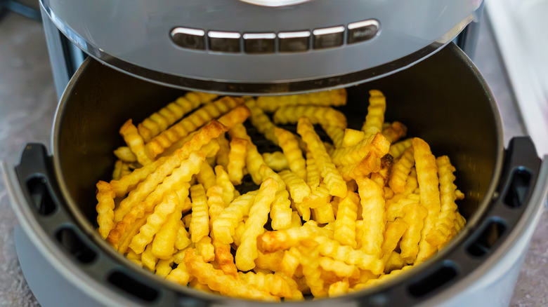 Cooked french fries fill the bottom of an air fryer basket.