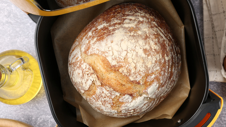 A round loaf of bread fills the opened parchment-lined drawer of an air fryer.