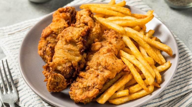 Plate of battered finger steaks with French fries served on clothed table with forks