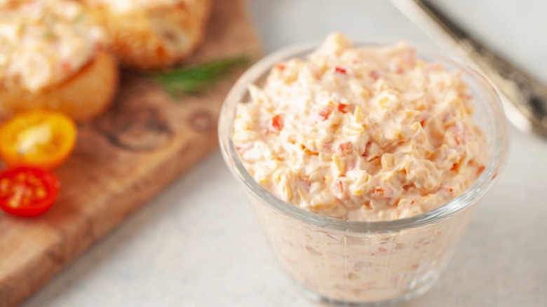 glass jar of pimento cheese with blurred slices of bread in the background
