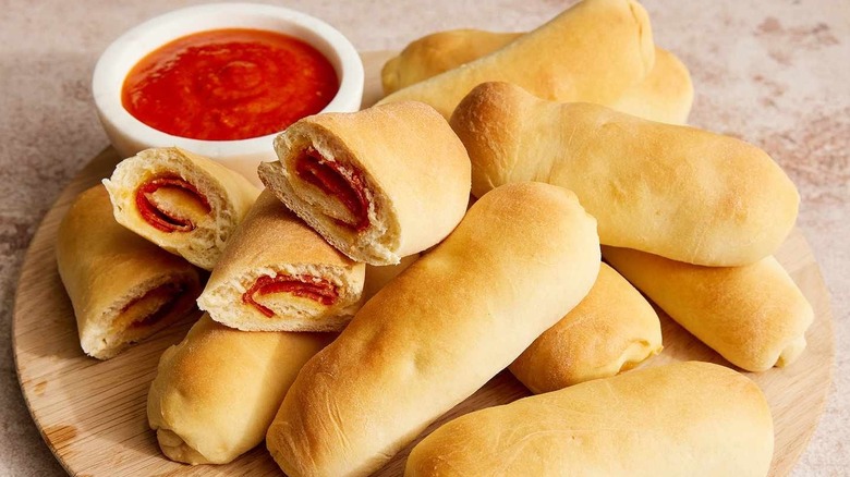 stack of pepperoni rolls on a wooden round with marinara sauce to the side