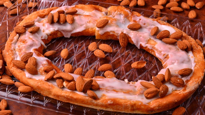 Kringle sitting on a glass dish with almonds scattered around