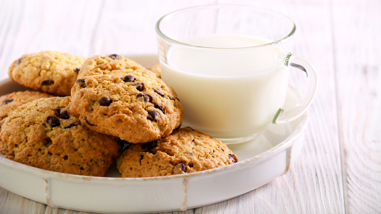 stack of cowboy cookies in a white dish with a glass mug of milk