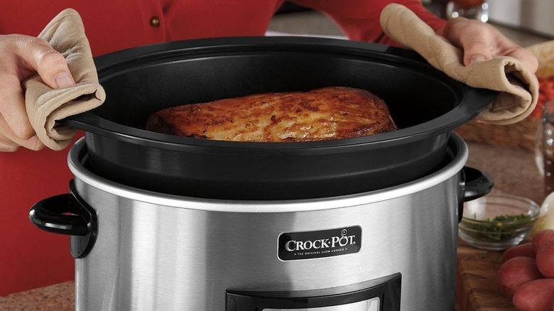 Hands lifting Crock-Pot insert with meat out of heating base.
