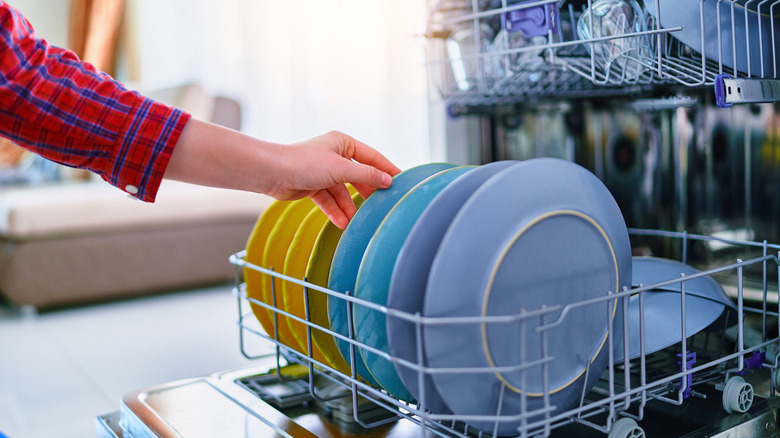An arm loads colorful plates into a dishwasher