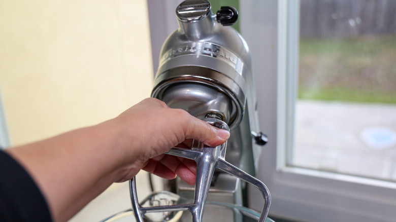 A hand grabbing the paddle attachment on a KitchenAid stand mixer