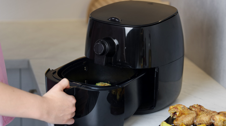 A hand pulls the drawer out of an air fryer.