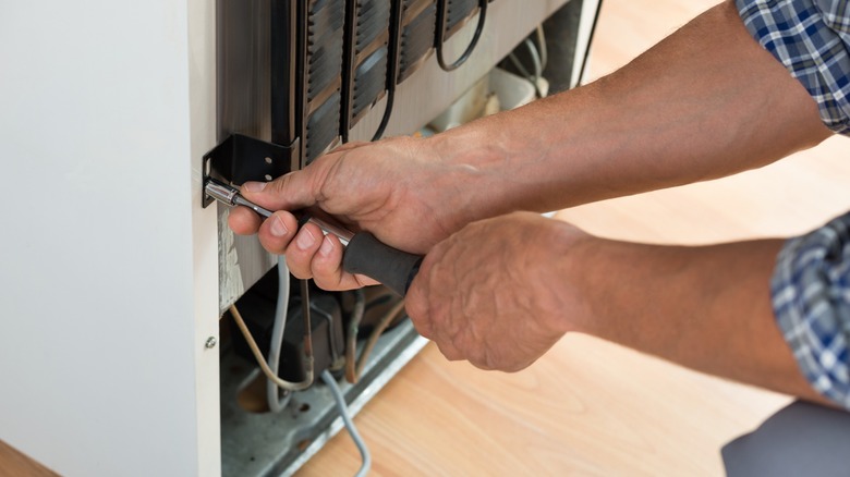 Repairman using tool to adjust bracket on back of refrigerator.