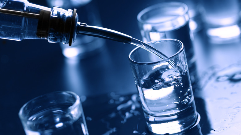 Liquor bottle with metal spout pouring vodka into shot glass.