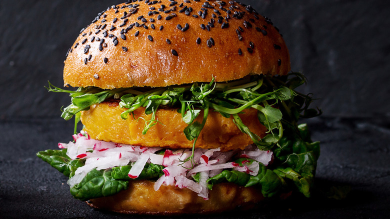 Close up of sweet potato burger on sesame seed bun with spinach, micro greens, and sliced onion