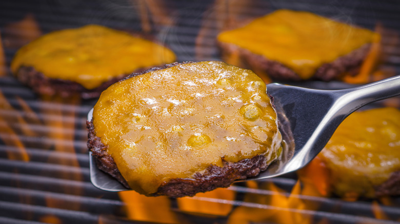 Spatula holds a cheeseburger patty in front of a grill with other cheeseburgers