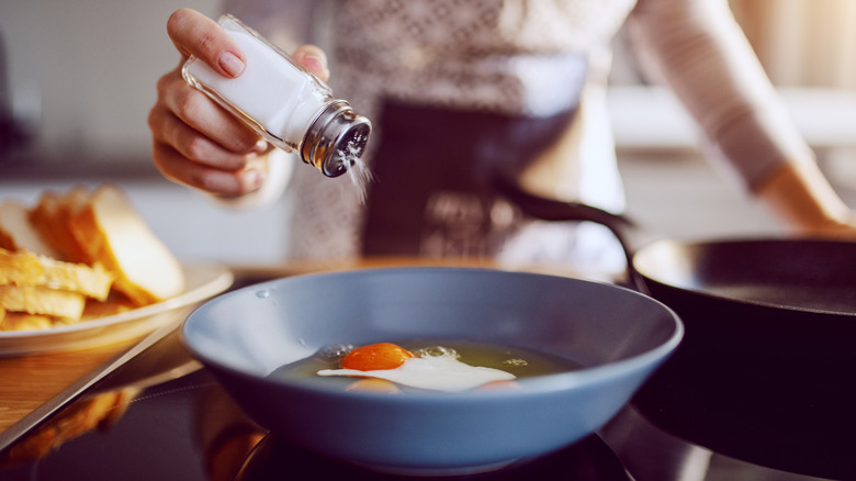 Home cook salting eggs in pan