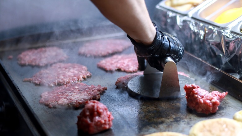 A cook smashes burgers on a hot griddle.