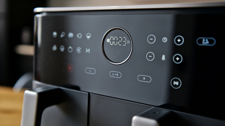 An air fryer control panel filled with a clock and other glowing icons.