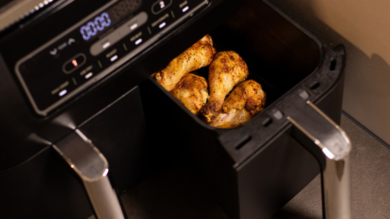 An air fryer with a lot of buttons, the drawer ajar to reveal chicken drumsticks.