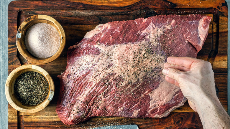 Hand sprinkling salt and pepper on uncooked brisket on cutting board
