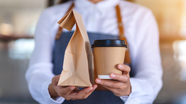 holding coffee and brown bag