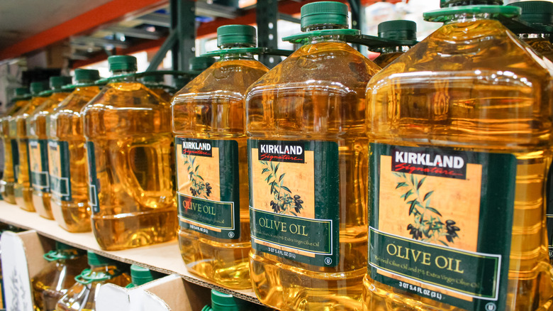 A row of Costco Kirkland Signature olive oil on a shelf in a Costco warehouse.