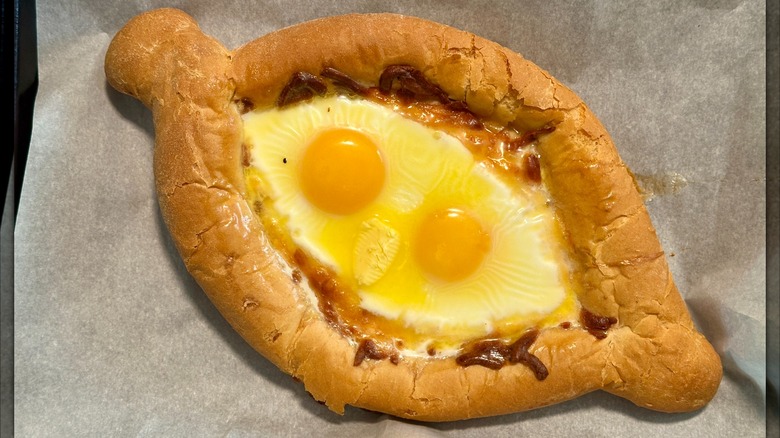 Khachapuri with two eggs on parchment paper.
