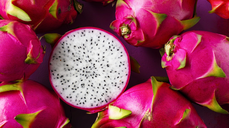 A cut dragon fruit with white flesh surrounded by whole pink fruits