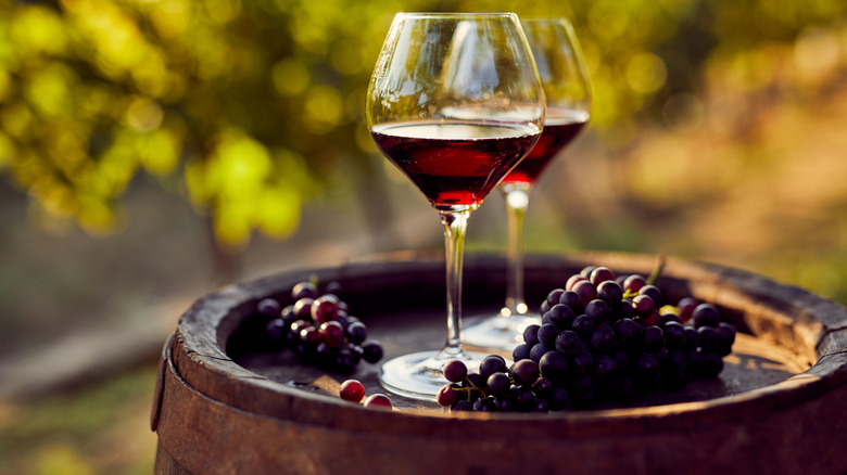Glasses of red wine on barrel with grapes