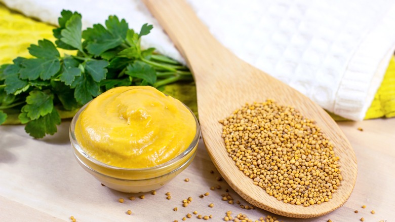 Spoonful of mustard seeds next to a bowl of mustard
