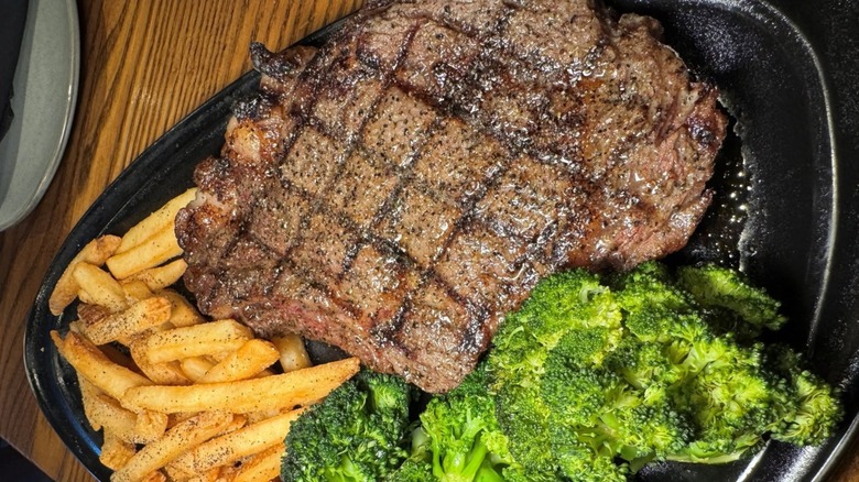 steak, fries, and broccoli on a black serving dish