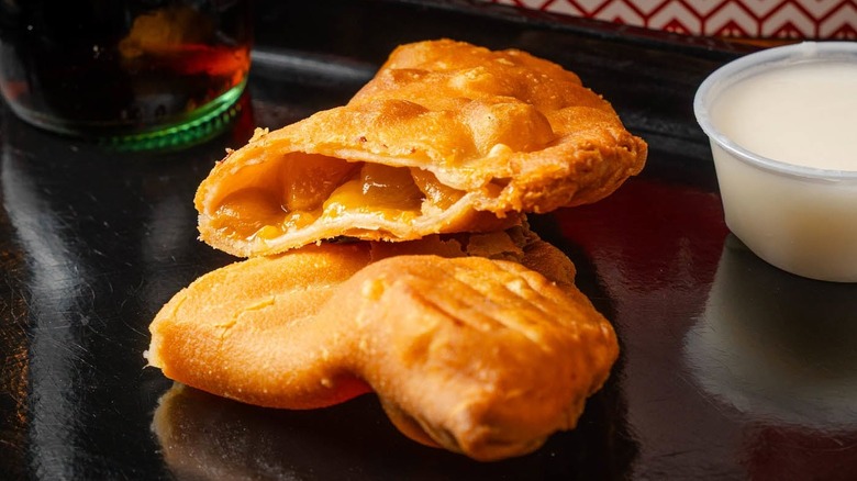 fried apple hand pie cut open, with white sauce on side