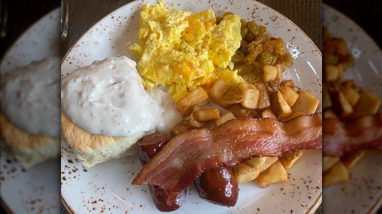 Home fries, bacon, eggs, biscuit and gravy on a plate.