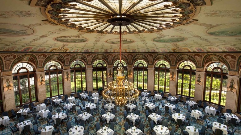 Grand interior of The Circle at The Breakers showing tables, chandelier, and large arched windows.