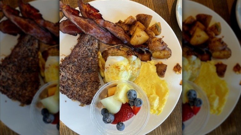 A plate of fruit, bacon, home fries, and more brunch items.