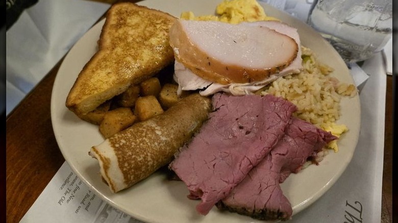 French toast, pancakes, home fries, sliced meats, on white plate.