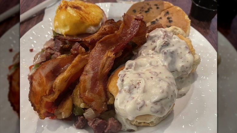 Bacon, biscuits and gravy, and more piled on white plate.