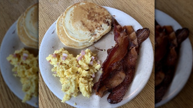 Eggs, bacon, and pancakes on white plate.