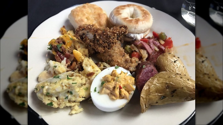 Potatoes, eggs, bagel, biscuit, deviled egg piled on white plate.