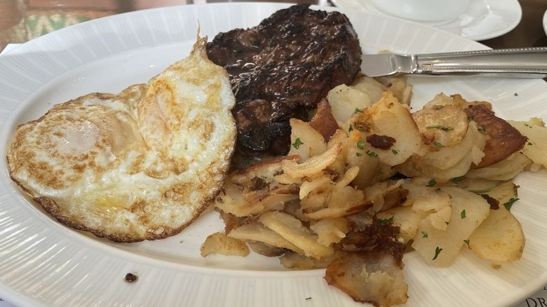 Steak, eggs, and potatoes on white plate.