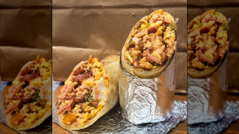 A breakfast burrito wrapped in aluminum foil and perfectly cut diagonally in half. The burrito is packed with eggs, bacon, jalapeños, roasted butternut squash, pintos charros, and quesadilla cheese