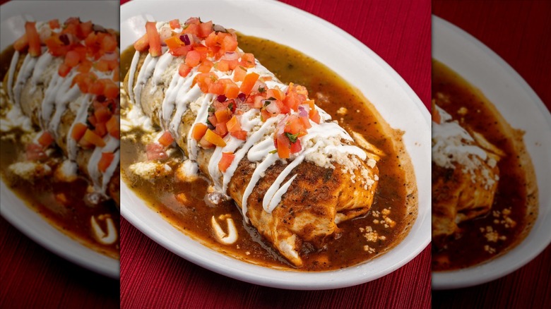 A whole smothered burrito with a drizzle of sour cream and pico de gallo on top