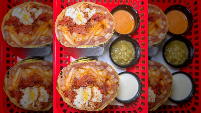 A breakfast burrito cut in half, filled with chorizo, eggs, cheese, beans, and fries, served with three sides in a red basket