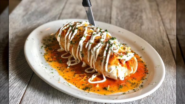 A breakfast burrito smothered with chipotle sauce, sour cream, and herbs on a white plate