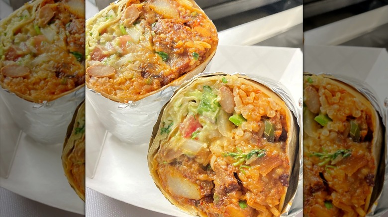 A breakfast burrito cut in half, filled with chicharron, chorizo, potatoes, jalapeños, rice, beans, pico de gallo, and cheese