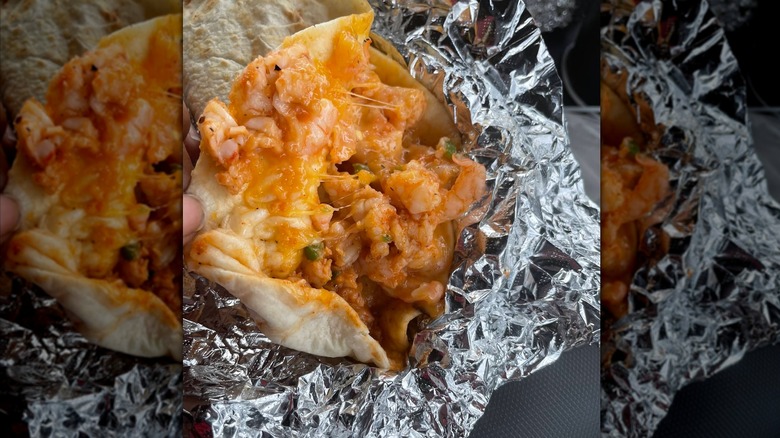 A foil-wrapped burrito opened to show its creamy contents