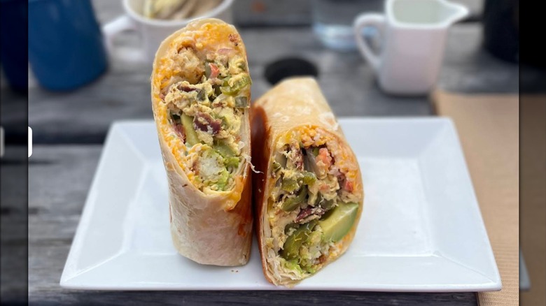 A breakfast burrito cut in half, filled with scrambled eggs, tater tots, and salsa fresca