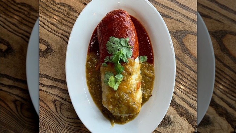 A smothered breakfast burrito topped with red and green chile sauces and cilantro