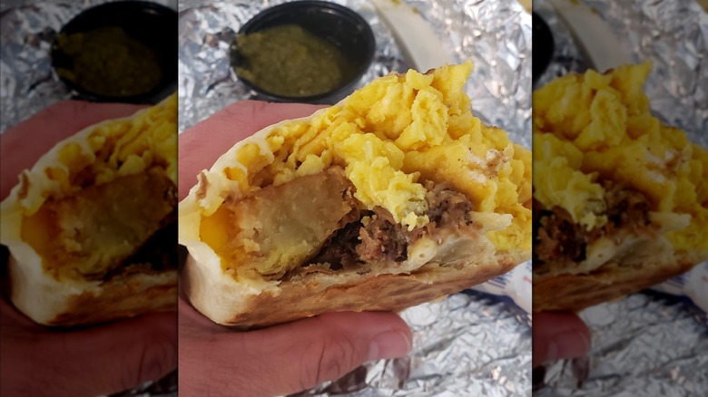 A breakfast burrito with a bite taken out of it, filled with eggs, cheese, and potatoes, served with with salsa on the side