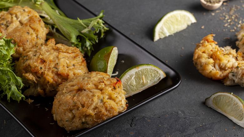 A black plate with crab cakes and lime wedges