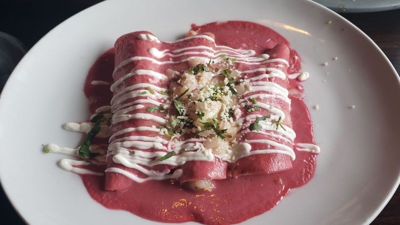 Three enchiladas on a white plate covered in pink sauce with drizzles of sour cream and a cheese and cilantro garnish