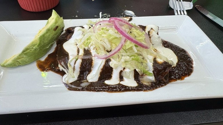Mole-covered enchiladas on a white plate drizzled with sour dream and topped with shredded lettuce