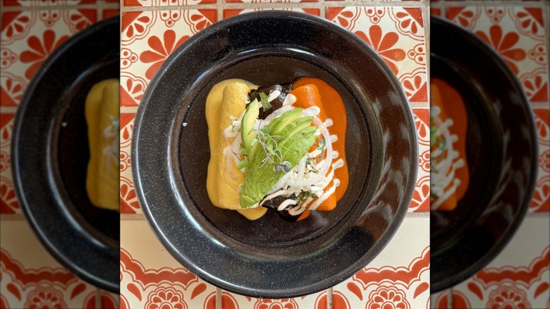 Three enchiladas on a black plate set on a vibrant orange-tile surface
