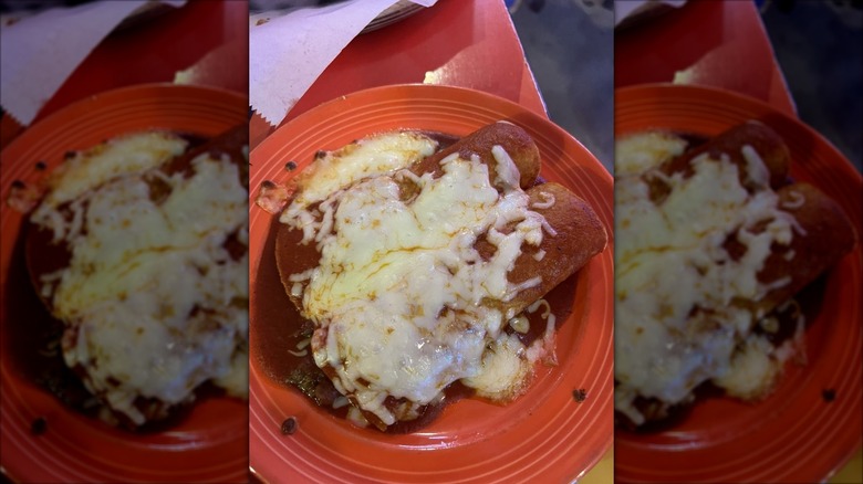 Two enchiladas wrapped in red tortillas on an orange plate covered in melted white cheese